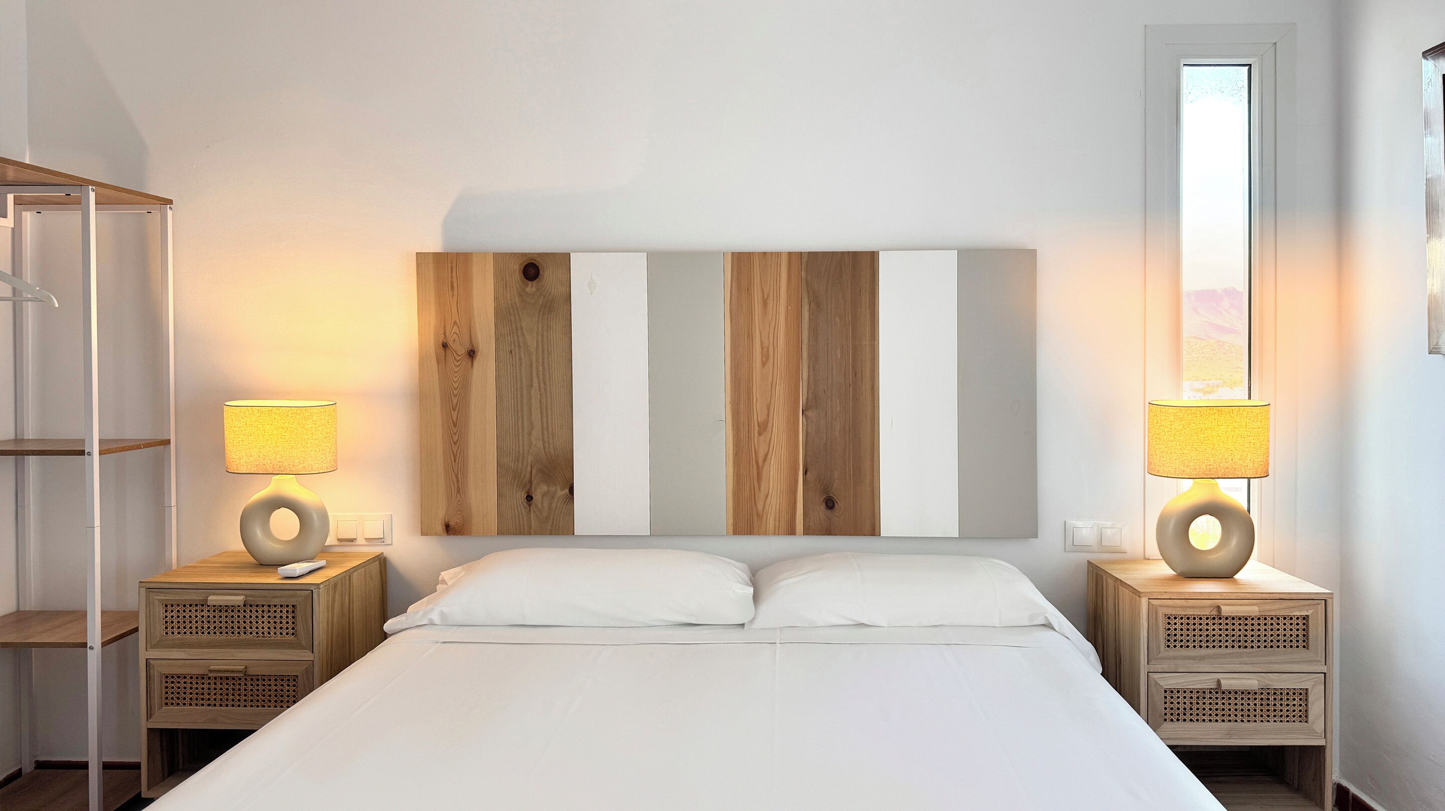 Una camera d'albergo con un letto grande, due comodini con lampade, una testiera in legno e un'ampia finestra.