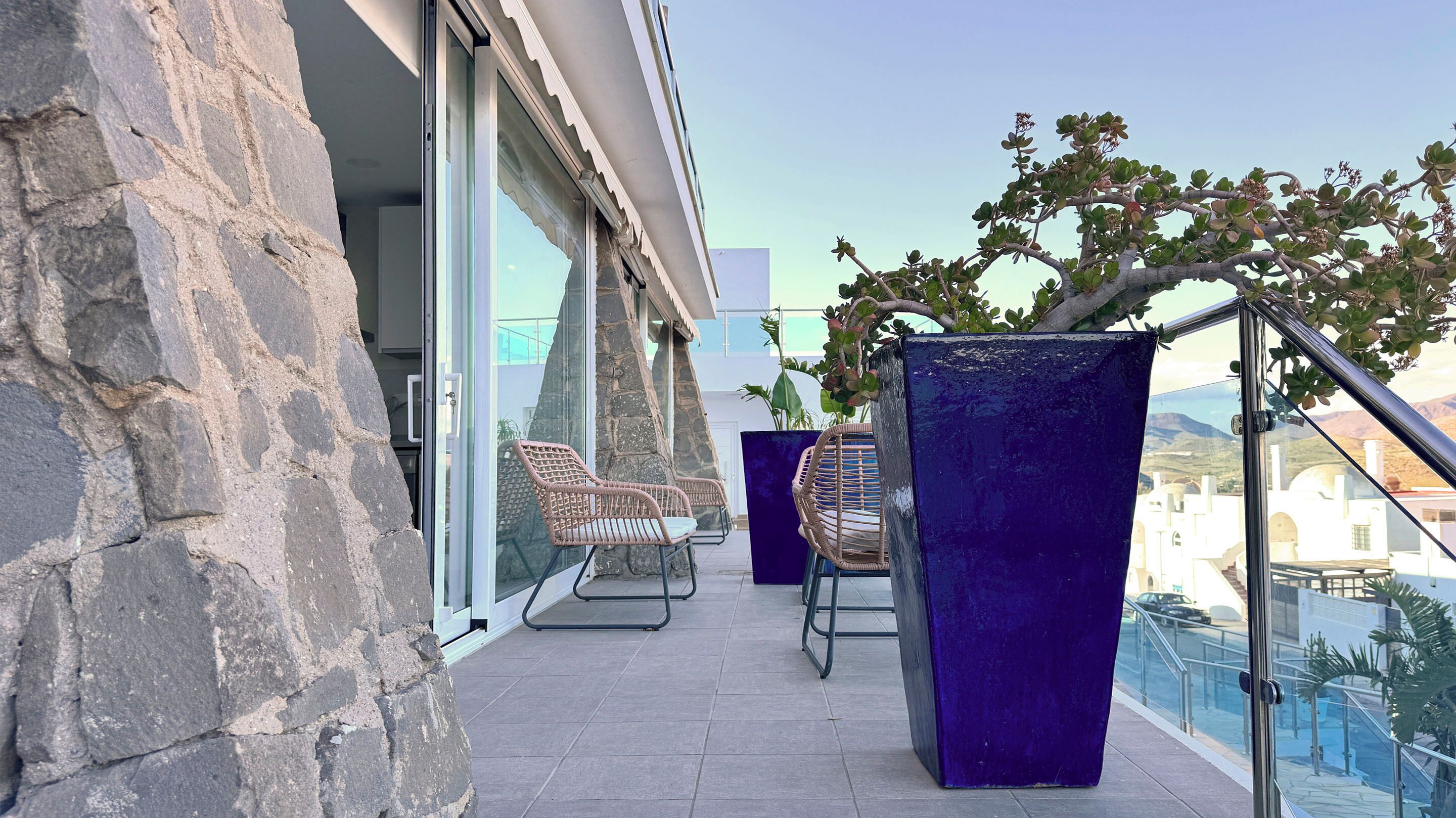 A balcony with stone walls, two wicker chairs, and a potted plant.