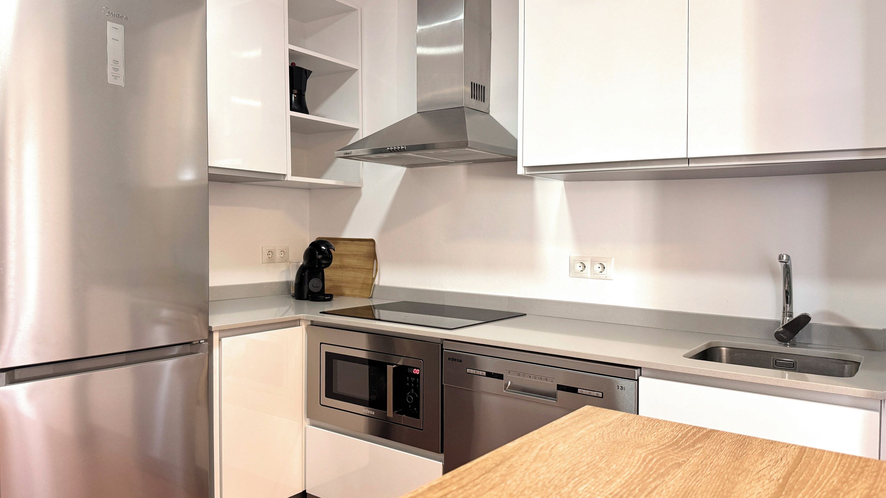 Een moderne keuken met roestvrijstalen apparatuur, witte kasten en een houten aanrecht.