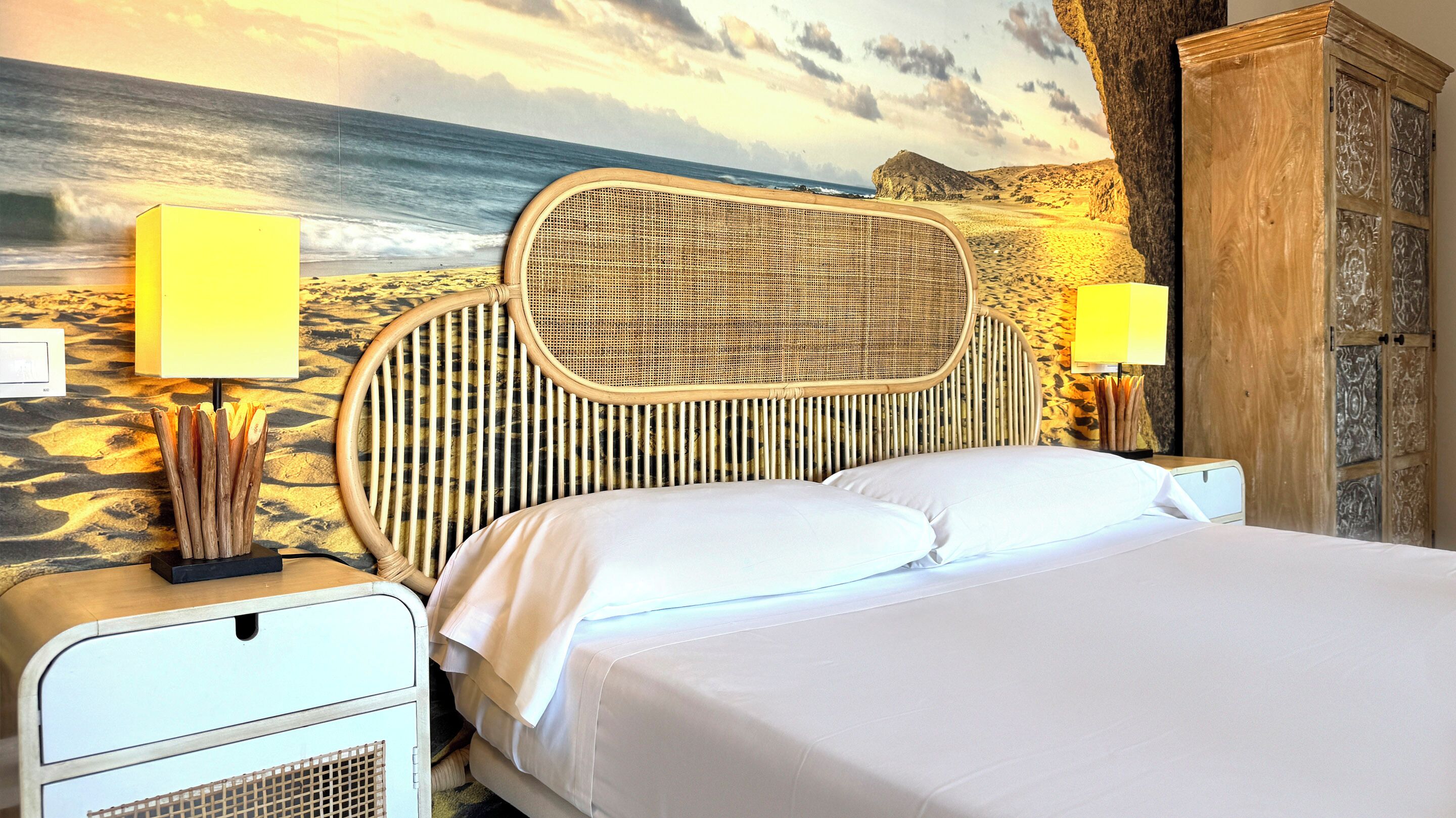 A bed with a woven headboard, two bedside lamps, and a wall mural of a beach scene.