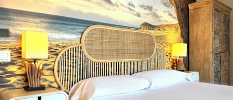 A bed with a woven headboard, two bedside lamps, and a wall mural of a beach scene.
