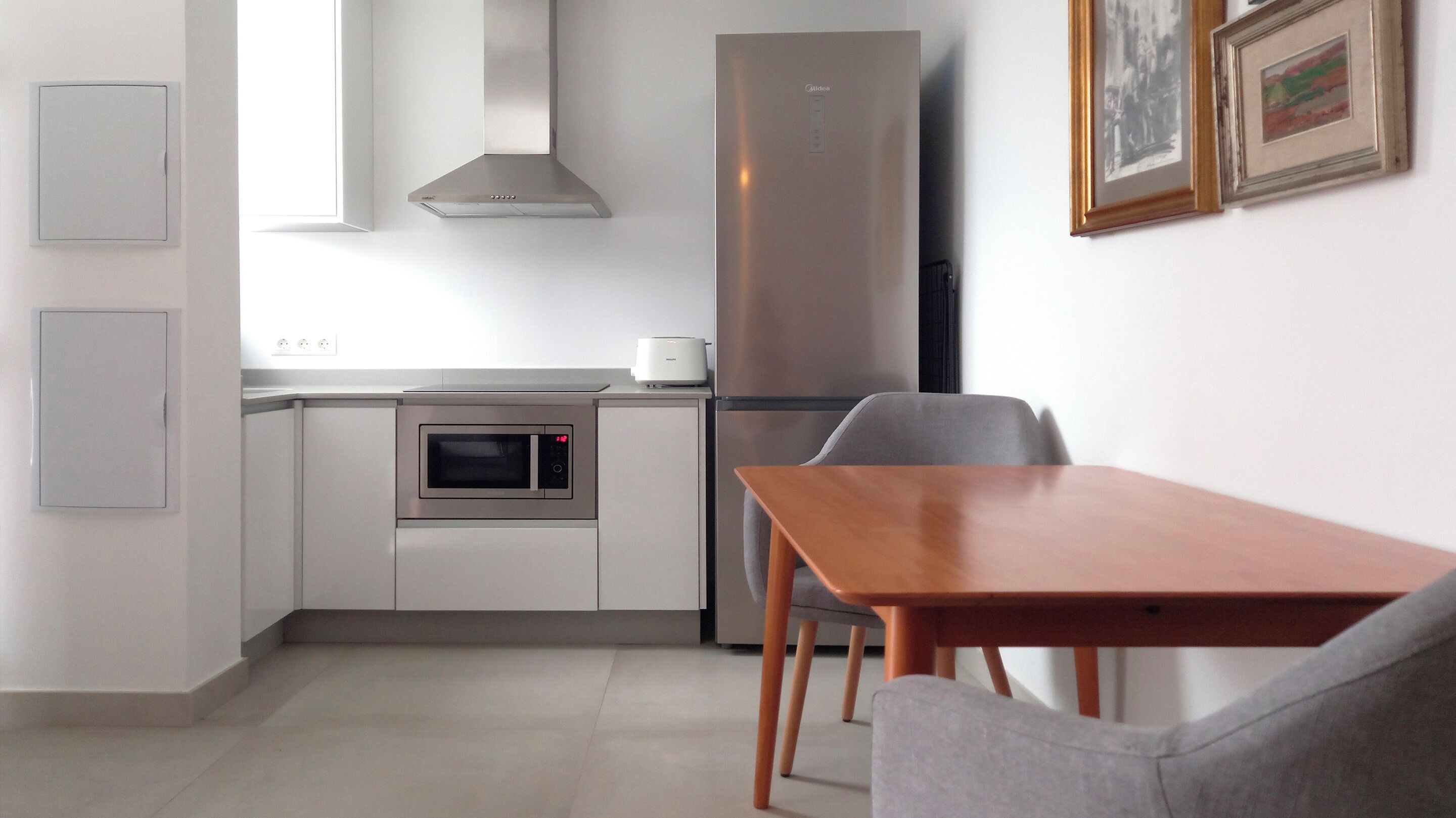 Eine moderne Küche mit Einbauofen, Edelstahlkühlschrank und einer Essecke mit Holztisch und zwei Stühlen.