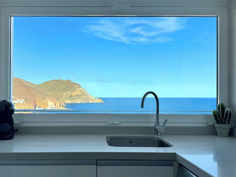 A kitchen with a large window overlooking a coastal landscape.