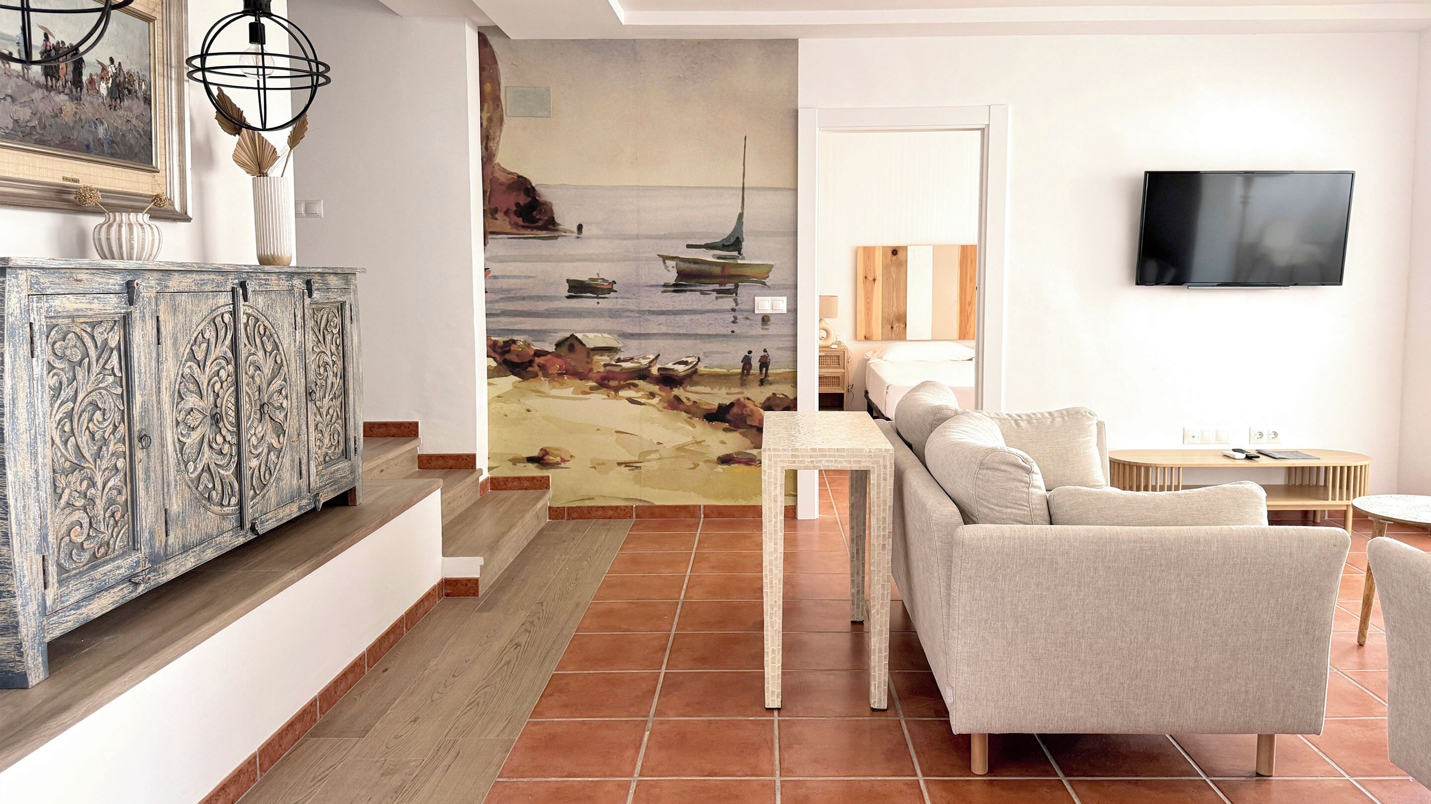 Un salón con sofá, televisión, un cuadro de barcos y una escalera.