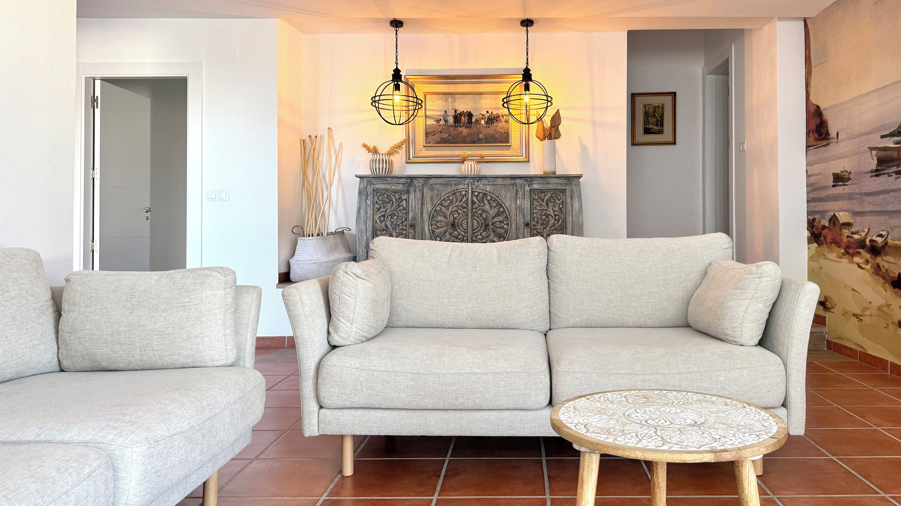 A living room with a grey sofa, a round wooden coffee table, and a decorative cabinet with a painting above it.