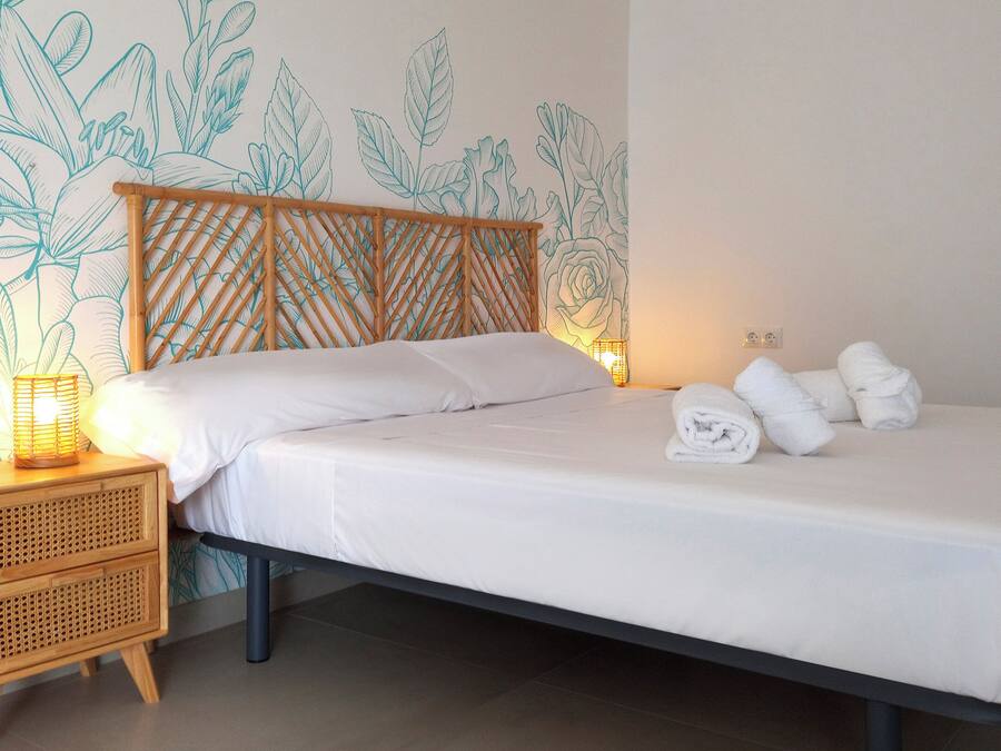 Una cama bien hecha con sábanas blancas, cabecera de madera y mesita de noche con lámpara.