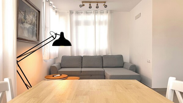 A modern living room with a wooden dining table, grey sofa, and a black floor lamp. - Apartamentos Julio Visconti (San José)