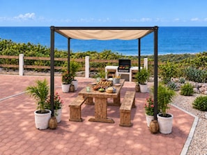 An outdoor patio with a wooden table and benches, a grill, and potted plants. - Spacious Serenity Suite · Sea Views · Infinity Pool & Jacuzzi · Walk to Beach (Vinoramas Diamante)