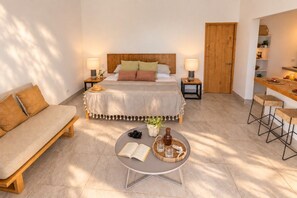 A hotel room with a bed, a sofa, a dining area, and a small table with a book and a camera. - Spacious Serenity Suite · Sea Views · Infinity Pool & Jacuzzi · Walk to Beach (Vinoramas Diamante)