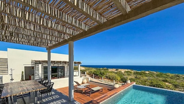 Area piscina con terrazza in legno, posti a sedere all'aperto e vista sull'oceano.
