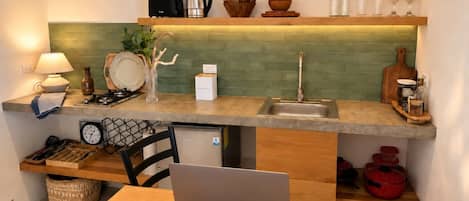 A compact kitchen with a laptop on the table, a coffee cup, and various kitchen utensils and appliances.