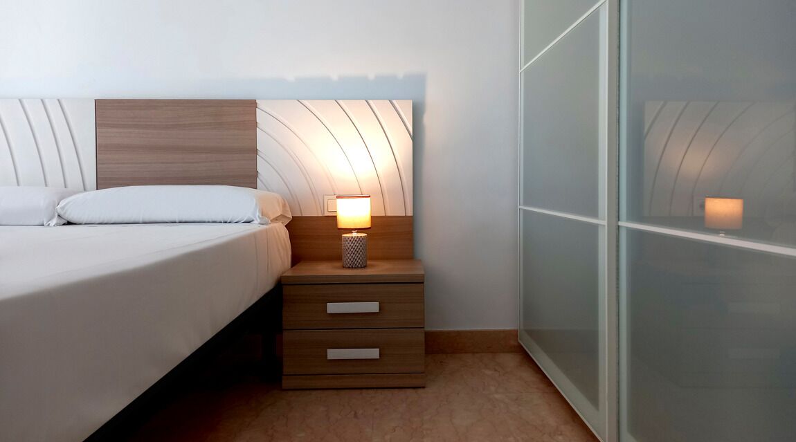 Un dormitorio con cama, mesita de noche con lámpara y armario con espejo.