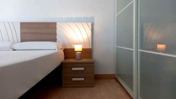Un dormitorio con cama, mesita de noche con lámpara y armario con espejo.