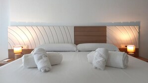 A hotel room with a large bed, two pillows, two bedside lamps, and two rolled towels on the bed. - Apartamentos Villa Azul (San José)