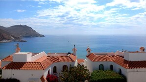 A coastal view with terracotta-roofed buildings overlooking the sea and a distant mountain. - Apartamentos Villa Azul (San José)