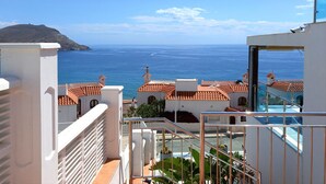 A coastal view from a balcony with terracotta roofs, a pool, and a clear view of the sea and a distant island. - Apartamentos Villa Azul (San José)