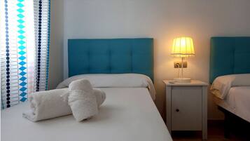 Habitación de hotel con dos camas, una mesita de noche con lámpara y una toalla enrollada sobre la cama.
