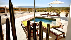 Ein Poolbereich mit Liegestühlen und Sonnenschirmen, umgeben von Kakteen.