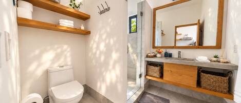 Un baño moderno con inodoro, estante y tocador con espejo.