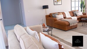 Un salon moderne avec un canapé en cuir marron, des coussins beige, une petite table basse ronde, un lampadaire et une œuvre d’art encadrée accrochée au mur.