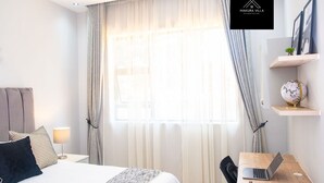 Une chambre d’hôtel moderne avec un grand lit, un bureau avec un ordinateur portable et un globe terrestre posé sur une étagère.