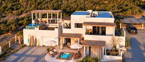 A modern two-story house with a swimming pool, outdoor seating, and a view of a desert landscape.