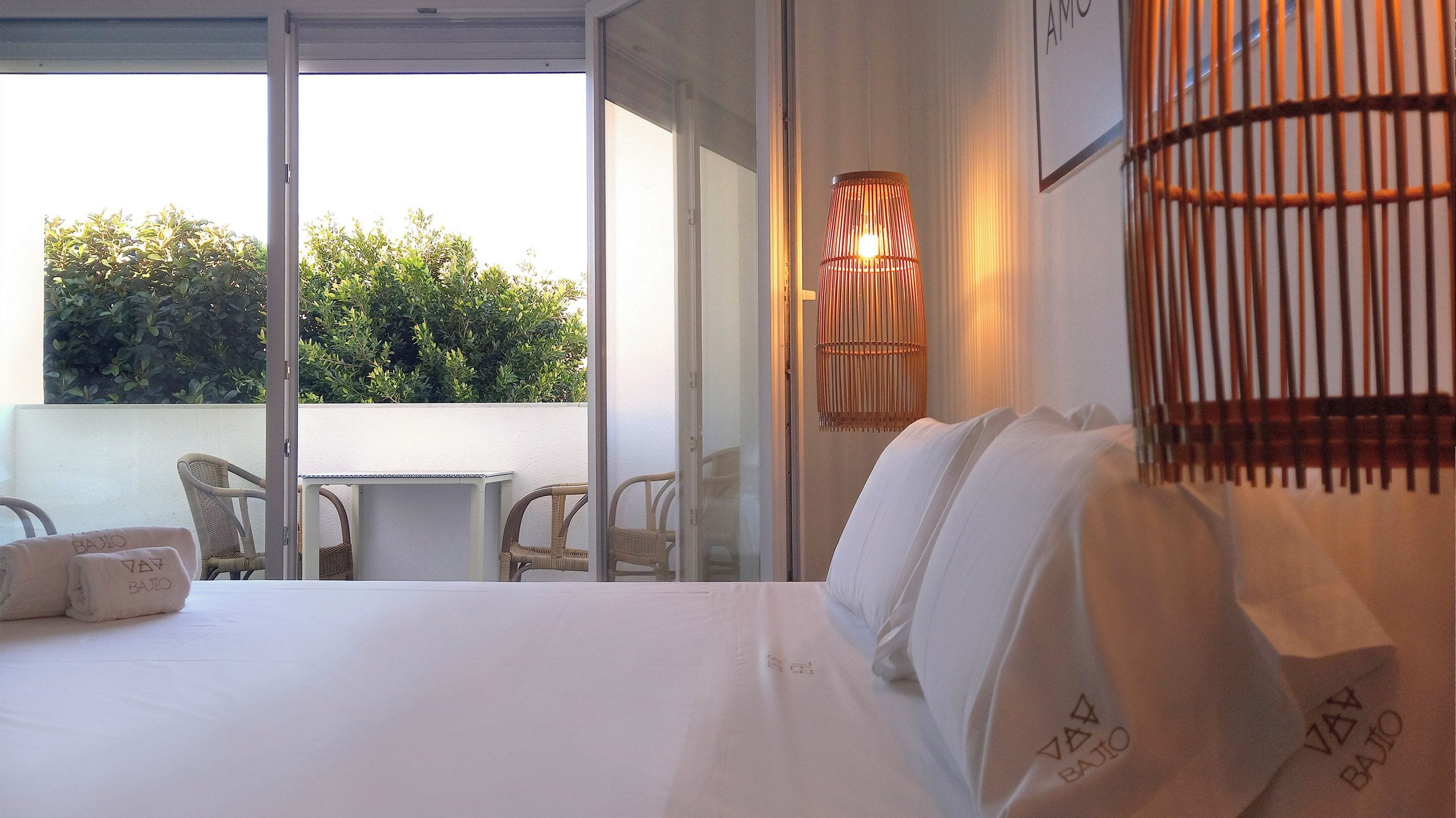 Une chambre d’hôtel avec un grand lit, une table et deux chaises. La fenêtre donne sur un paysage verdoyant.