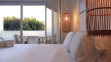 Une chambre d’hôtel avec un grand lit, une table et deux chaises. La fenêtre donne sur un paysage verdoyant.