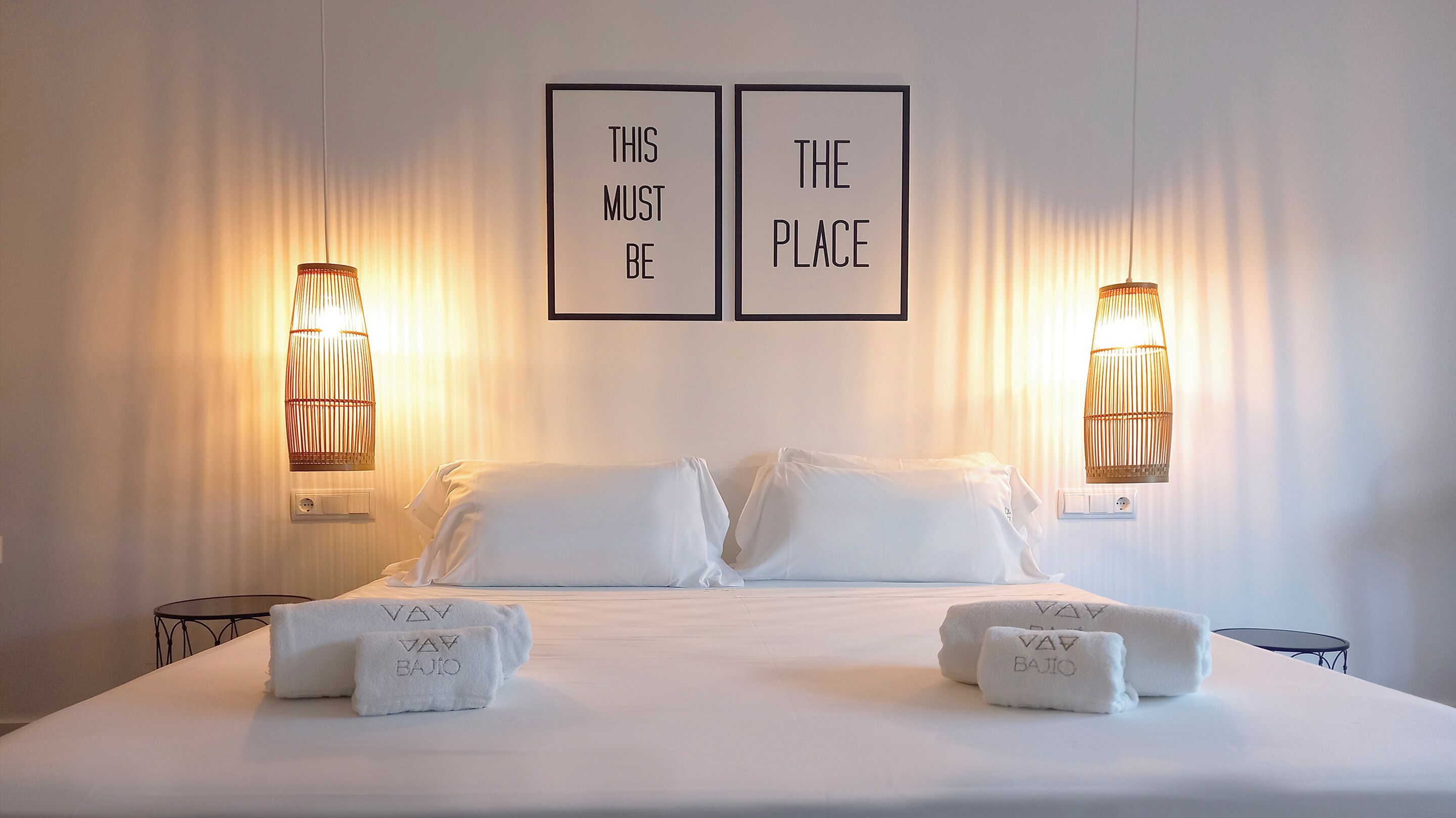 A hotel room with a bed, two wall-mounted lamps, and two framed motivational quotes.