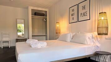 A neatly made bed with white linens and towels, a bedside table, a chair, a wardrobe, and two wall-mounted lamps.
