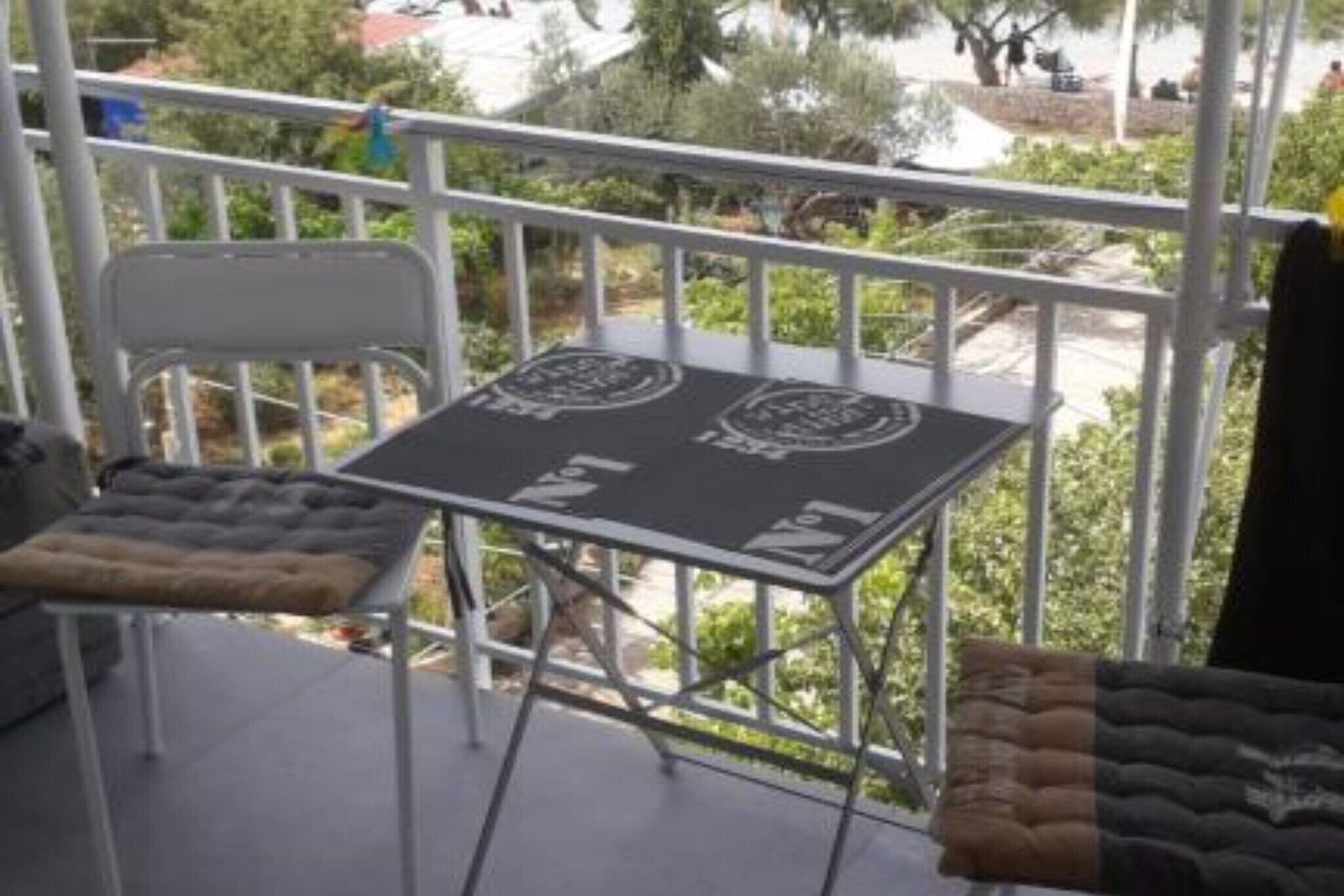 A balcony with a metal table and chairs, a view of the surrounding area, and a railing.