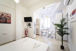 A hotel room with a bed, a desk, a chair, a television, a fire extinguisher, and a potted plant.