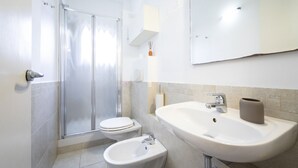 A bathroom with a shower, toilet, bidet, sink, and mirror. - Sarpi Flat (Firenze)