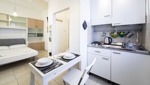 A compact hotel room with a bed, a small dining table with plates and glasses, a kitchenette with a stove and sink, and white cabinets. - Sarpi Flat (Firenze)