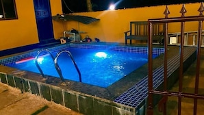 A rectangular swimming pool with a metal ladder, surrounded by a tiled deck and a metal gate. - Karma Stays Hostel Morjim (Morjim)