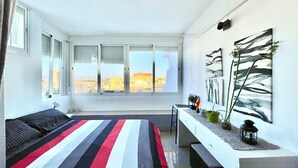 Un dormitorio moderno con una cama grande, un escritorio y vistas de la ciudad a través de amplias ventanas.