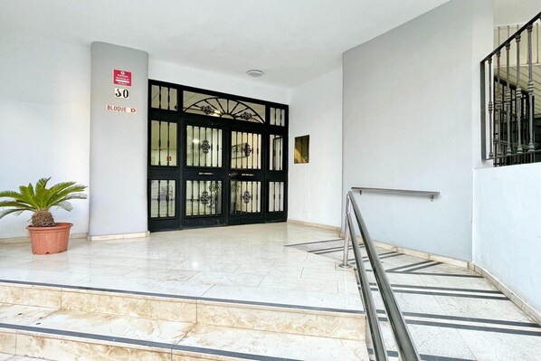 A building entrance with a black gate, a potted plant, and a staircase with a handrail.