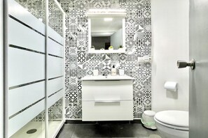 A bathroom with a white sink, a mirror, and a toilet. The walls are decorated with patterned tiles.