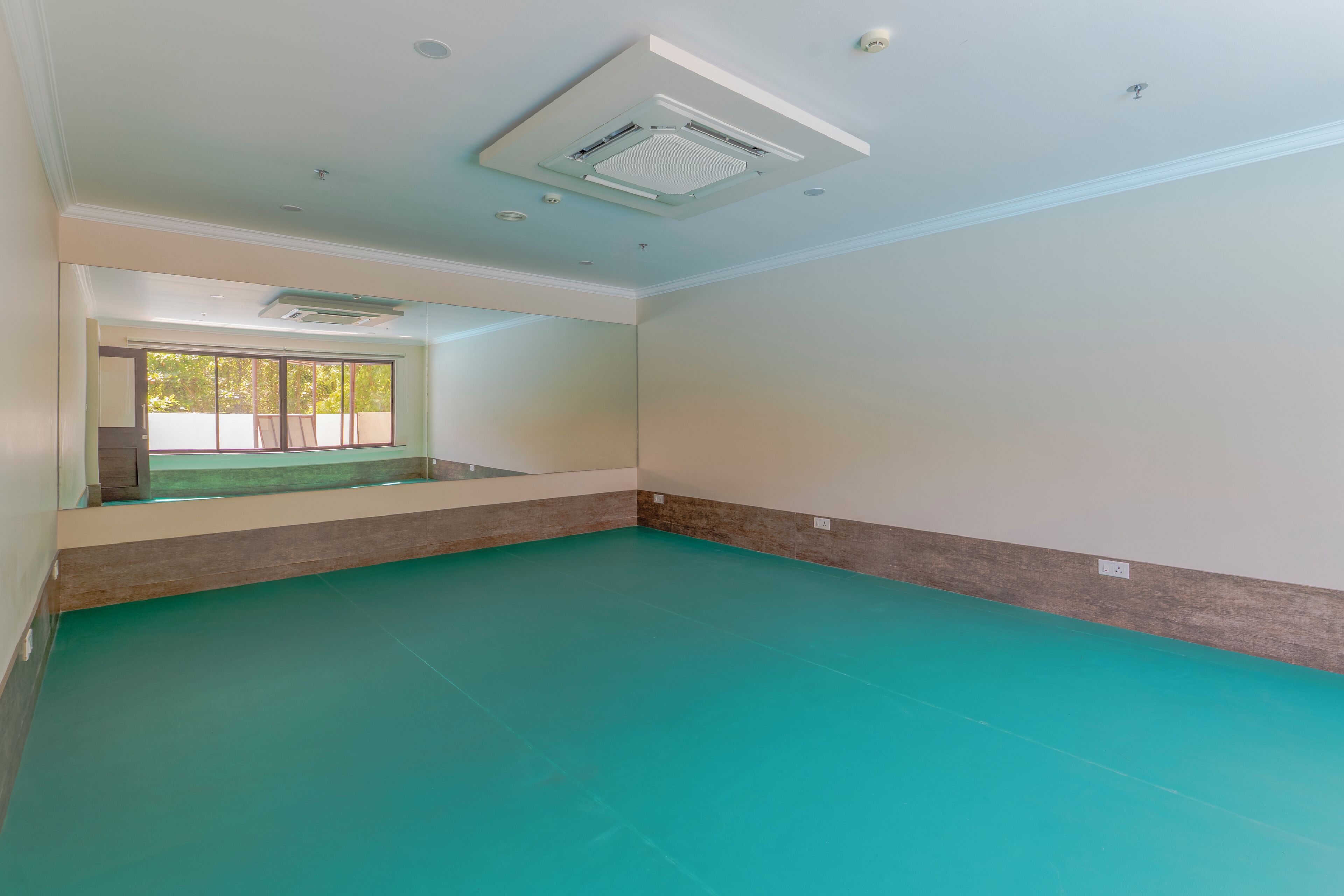 Ein geräumiges Zimmer mit großem Fenster, einer Decken-Klimaanlage und einem turquoisefarbenen Boden.