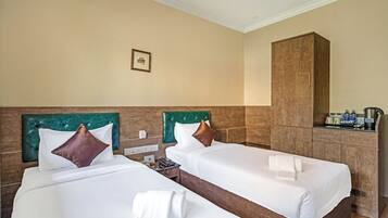 Habitación de hotel con dos camas, cada una con cabecera, ropa de cama blanca y almohada marrón. Hay un mueble de madera y una mesita con un teléfono y una botella.
