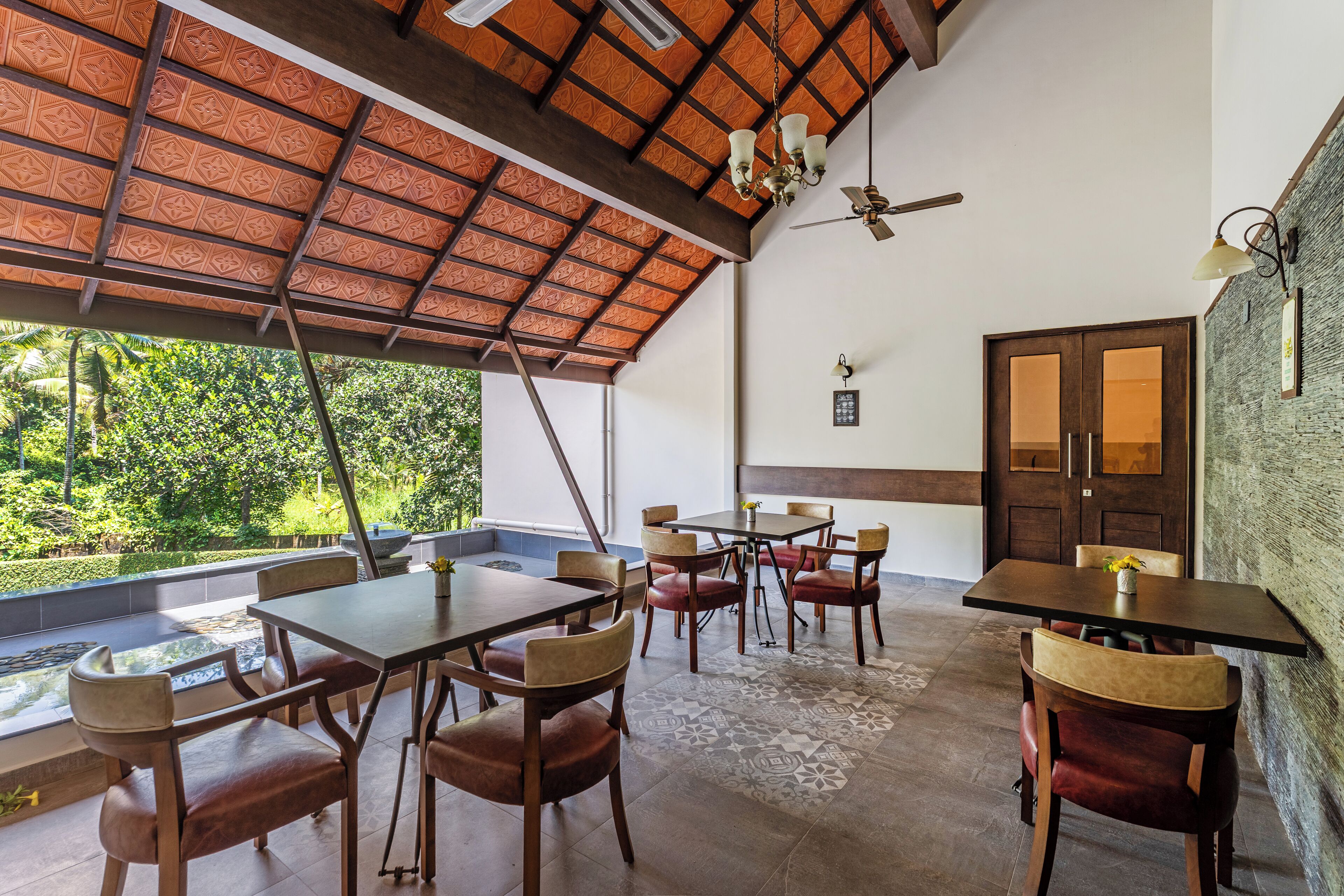 A dining area with wooden tables and chairs, a ceiling fan, and a view of greenery outside.