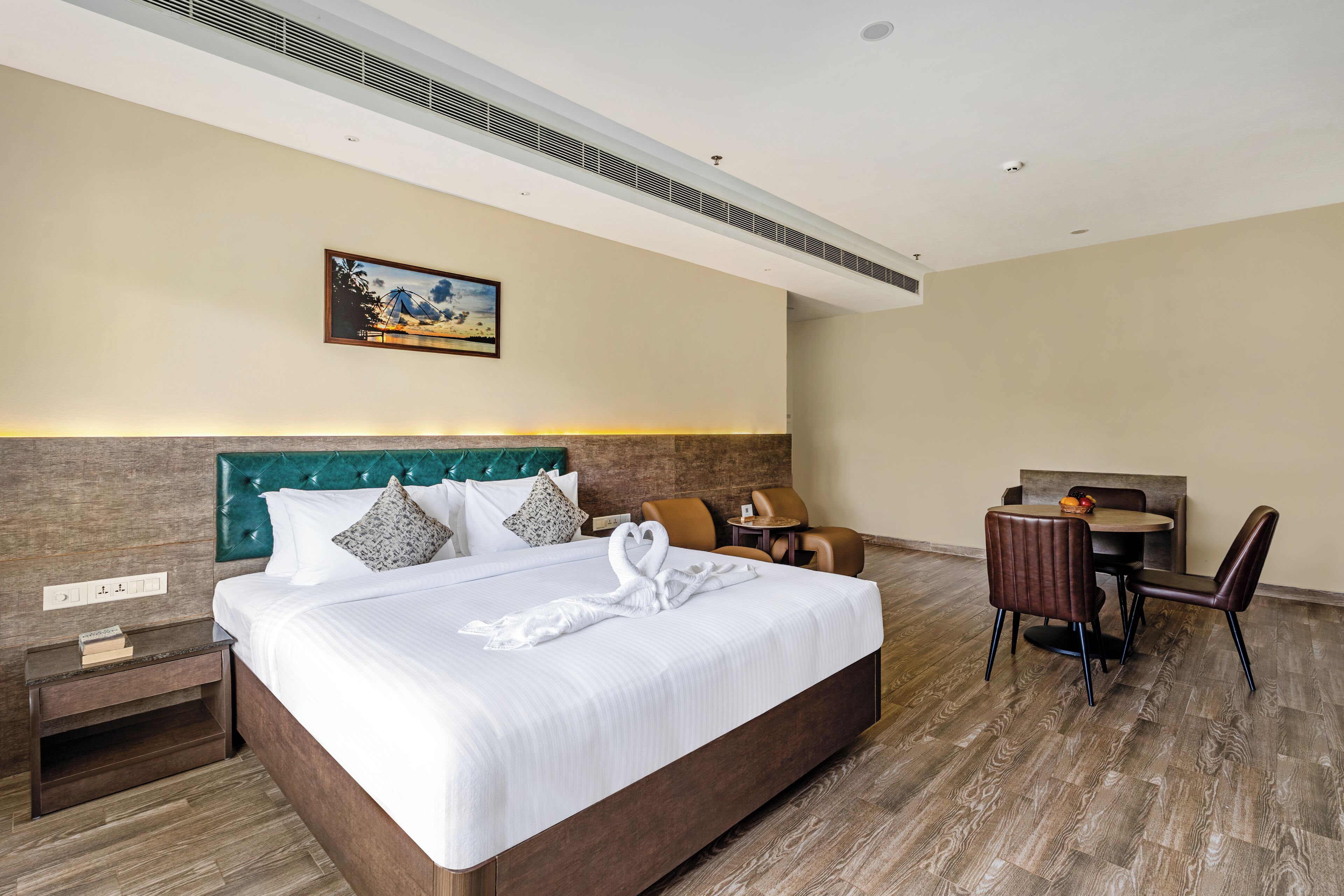 A hotel room with a large bed, a desk with two chairs, a small table, and a painting on the wall.