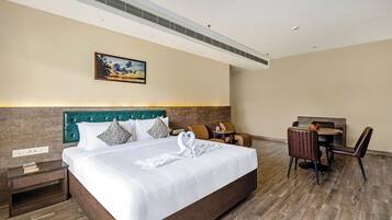 A hotel room with a large bed, a desk with two chairs, a small table, and a painting on the wall.