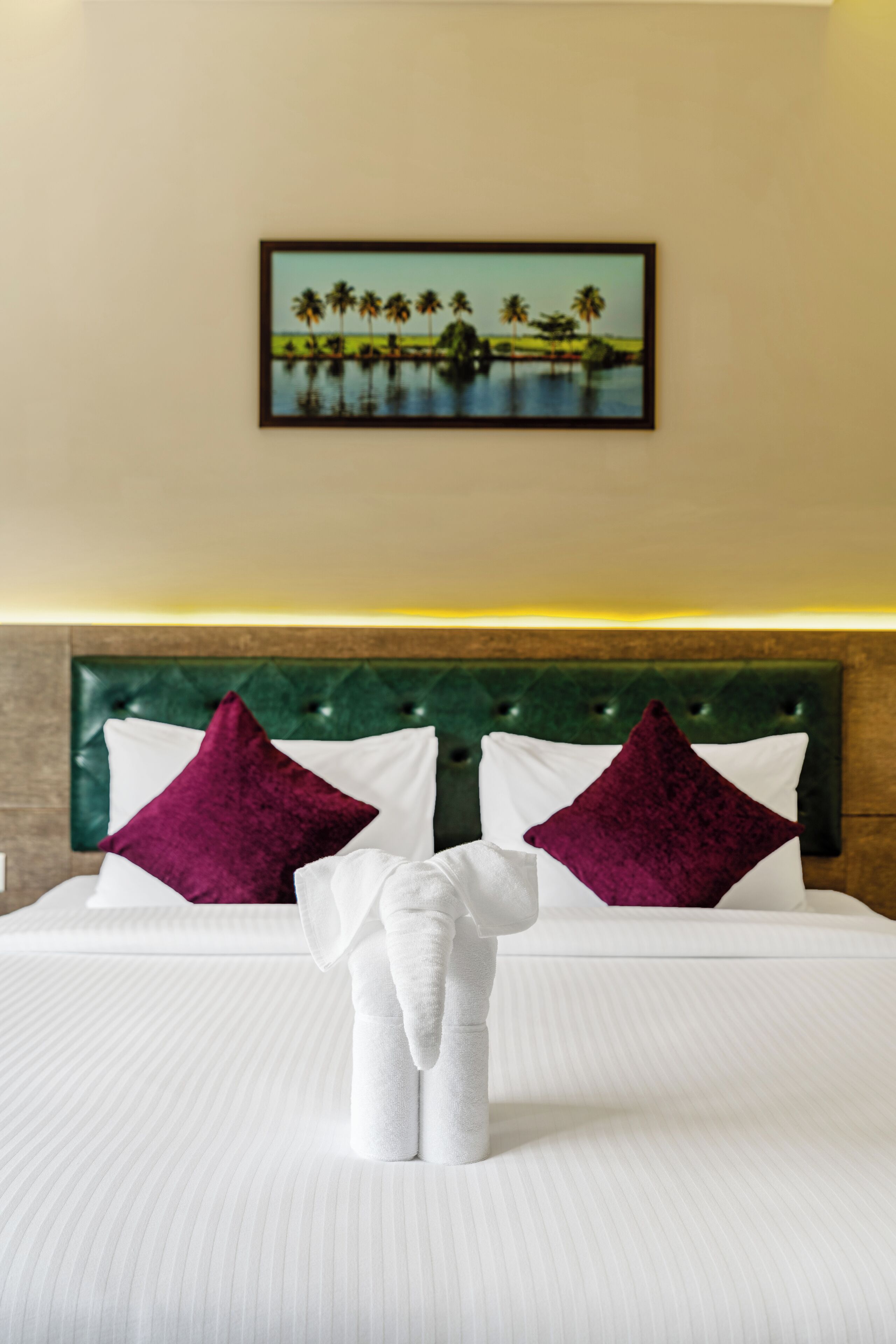 Habitación de hotel con cama, dos almohadas, cabecero y un cuadro en la pared.