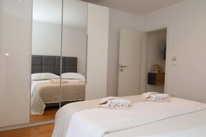 A bedroom with a bed, a wardrobe, a mirror, and a door leading to another room. - Dalmata D - Two Bedroom Apartment with Terrace (Podstrana)
