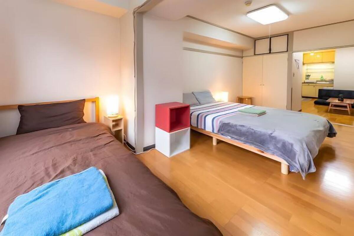 Una habitación con dos camas, un escritorio pequeño y una kitchenette al fondo.