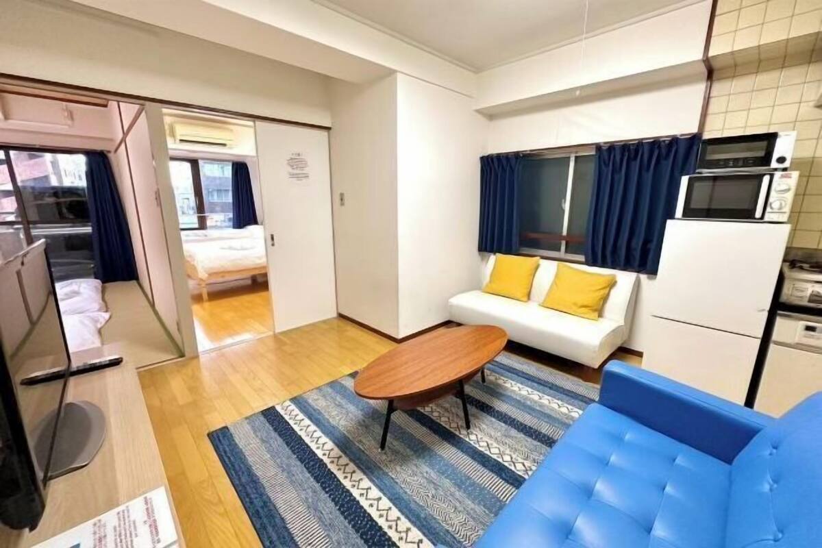 Una habitación compacta con cama, sofá, una mesita, microondas y refrigerador.