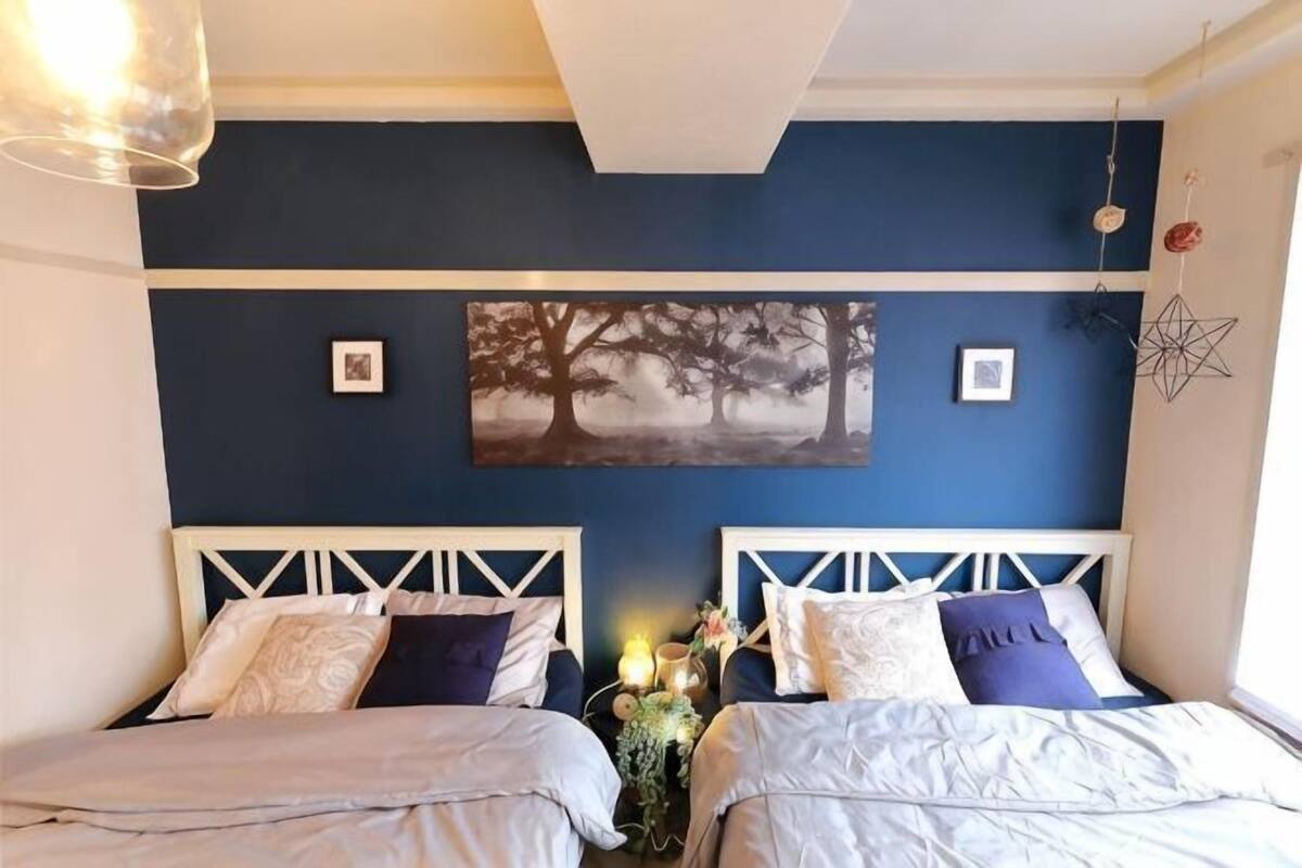 Un dormitorio con dos camas, una pared azul decorativa y una obra enmarcada sobre las camas.