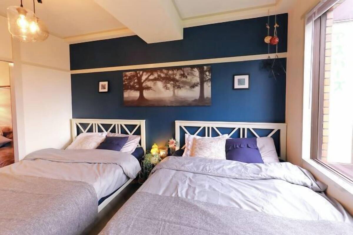 Una habitación con dos camas, una lámpara en el techo, un cuadro en la pared y una ventana.