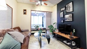 A living room with a ceiling fan, a sofa, a coffee table, a TV, and framed pictures on the wall. - Yotsuya Matsumoto Hotel (Tokyo)